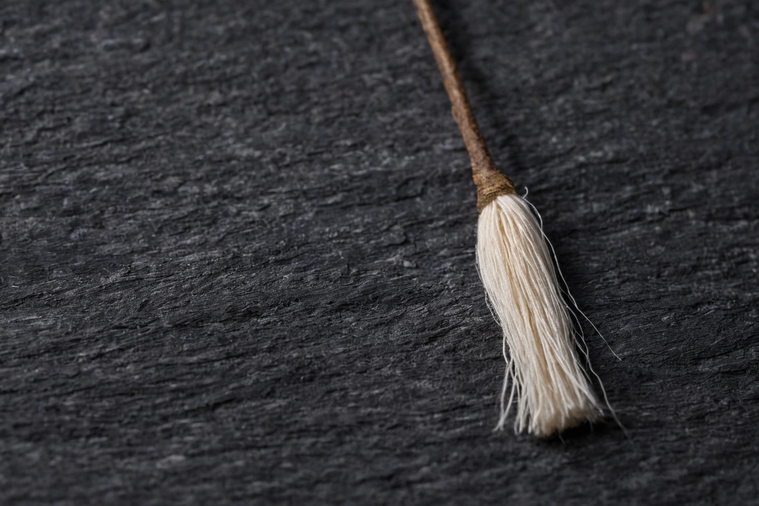 Extreme macro photograph of a single crimped wool fibre with overlapping cuticle scales on a dark slate tile